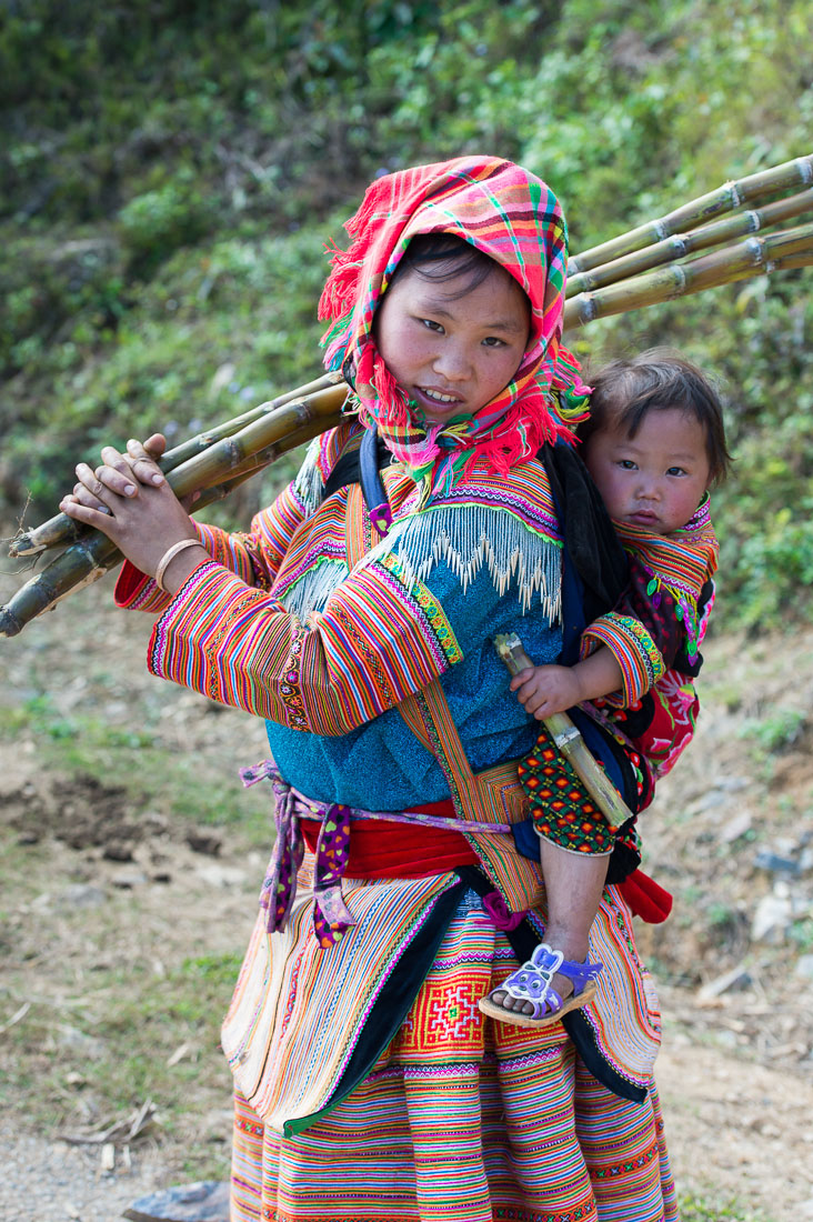 Young mother from the Red Hmong people ethnic minority, carrying her baby, wearing traditional costume, countryside Ha Giang province. Viet Nam, Indochina, South East Asia.