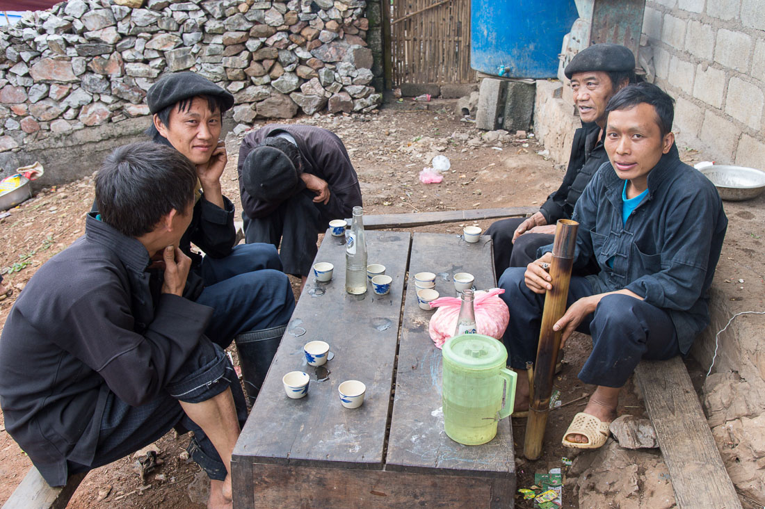 A group of man from the Black Hmong people ethnic minority group, wearing the traditonal berret, having a smoke and few shots of what they call whiskey a spirit distilled from rice. Lung Pin market, Ha Giang province, Viet Nam, Indonesia, South East Asia