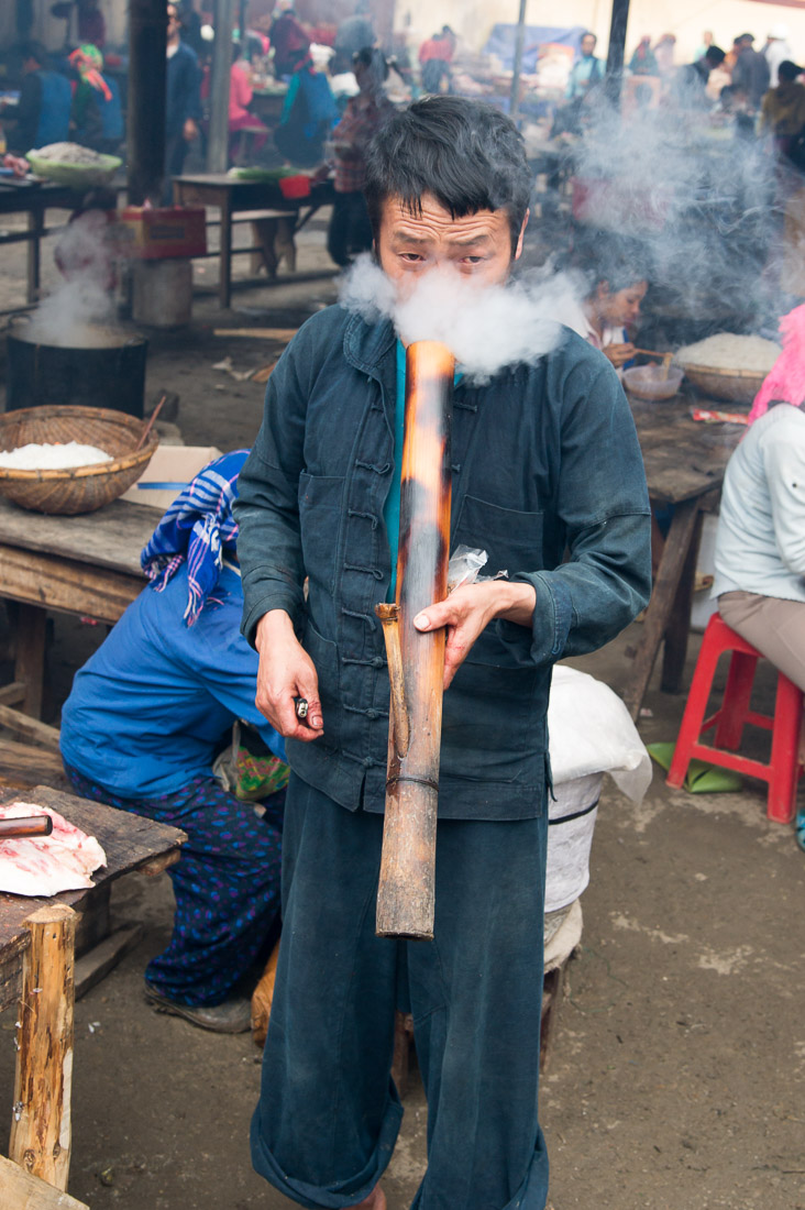 Young man from the Black Hmong people ethnic minority group, wearing the traditional costume, taking a strong puff from his bamboo bong. Meo Vac market, Ha Giang province, Viet Nam, Indonesia, South East Asia