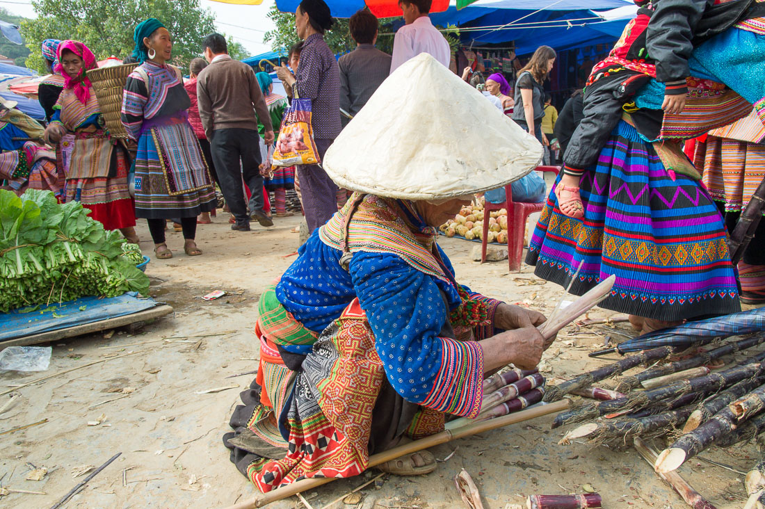 An old woman from the Flower Hmong people ethnic minority wearing the traditional costume and bamboo hat cleaning sugar cane, Bac Ha market, Lao Cai Province, Viet Nam, Indochina, South East Asia