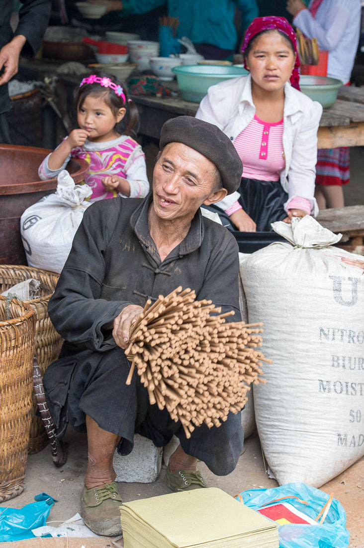 Man from the Flower Hmong people ethnic minority group, wearing his traditional beret, selling incense burning sticks at busy market in Lung Phin, Ha Giang Province, Viet Nam, Indochina, South East Asia