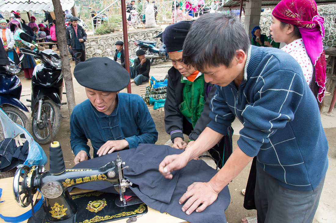 A taylor from the Flower Hmong people ethnic minority group, wearing his traditional beret, working with his Chinese  sewing machine at busy market in Lung Phin, Ha Giang Province, Viet Nam, Indochina, South East Asia