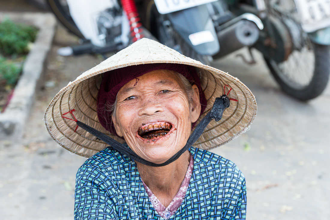 Old woman, smiling and showing her stained teeth and lips because of her addiction of chewing paan (lime, tobacco, areca nuts and betel leaves). Hoi An market, Quang Nam province, Viet Nam, Indochina, South East Asia.