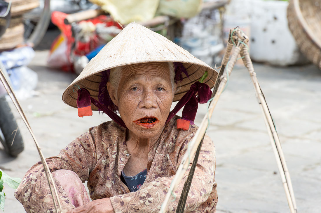 Old woman, smiling and showing her stained teeth and lips because of her addiction of chewing paan (lime, tobacco, areca nuts and betel leaves). Hoi An market, Quang Nam province, Viet Nam, Indochina, South East Asia.